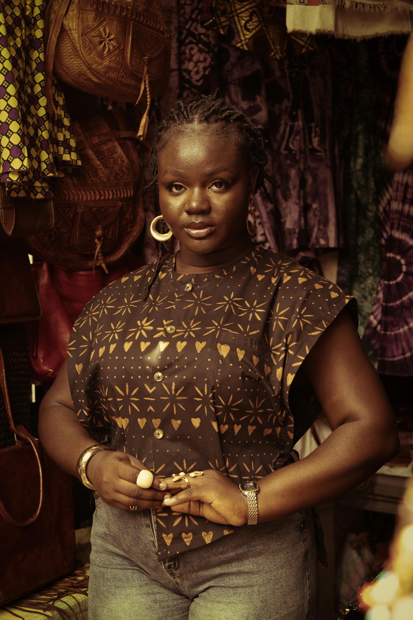 A woman in a printed blouse and jeans poses confidently in an artisan market.