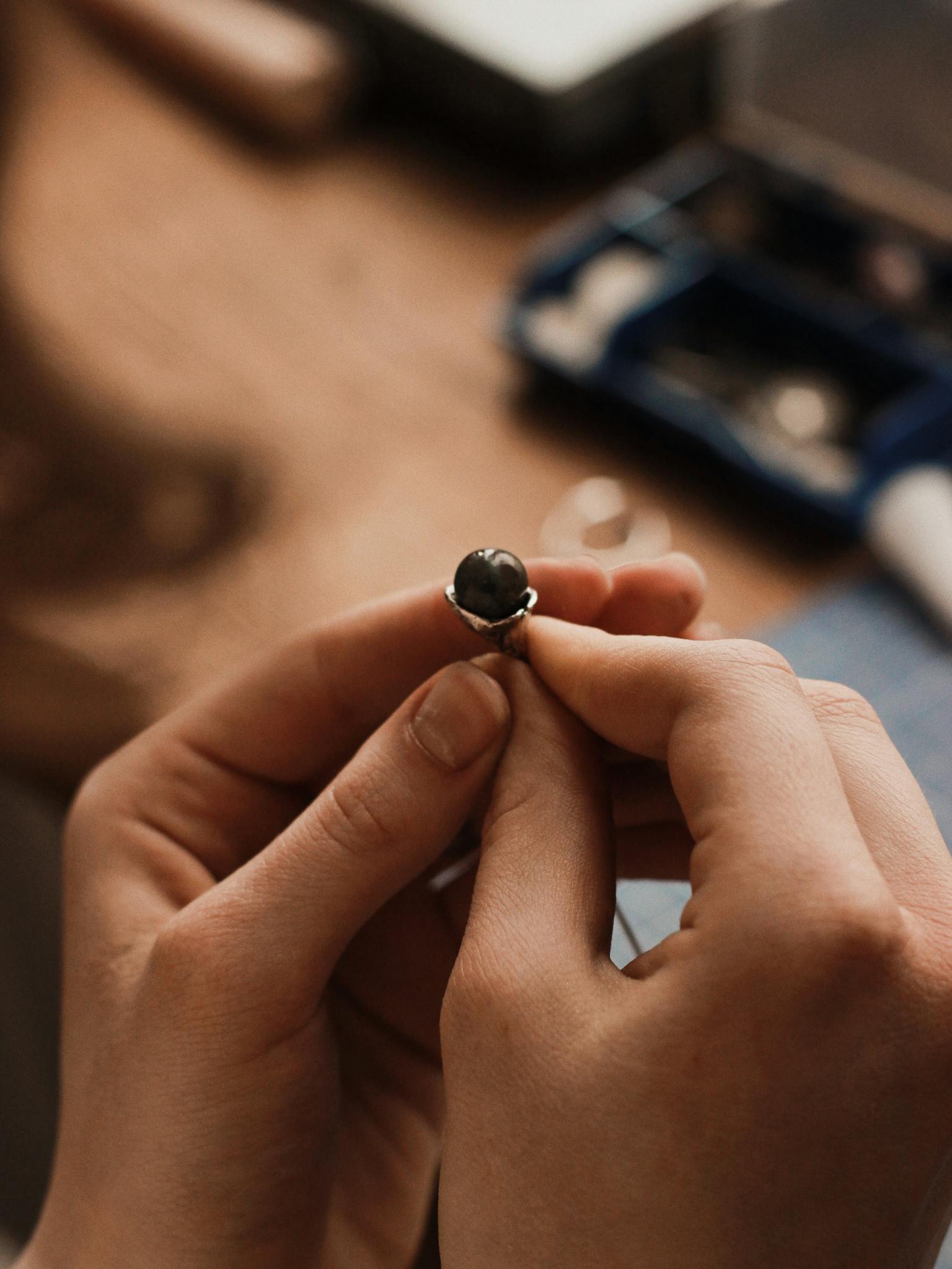 Close-up of hands crafting a silver ring, featuring dark stone. Artistic jewelry making.