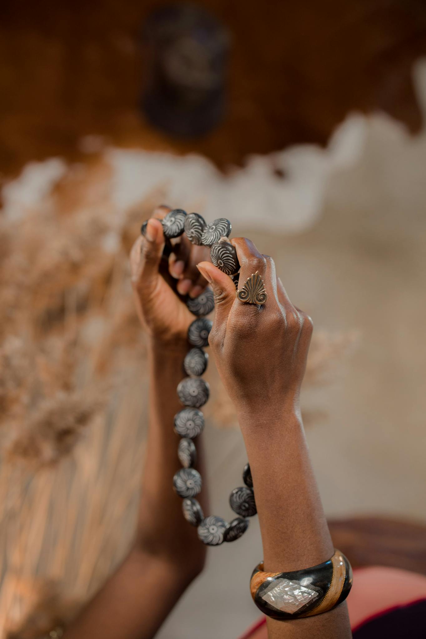 Close-up of hands holding an ornate handcrafted necklace against a blurred background.